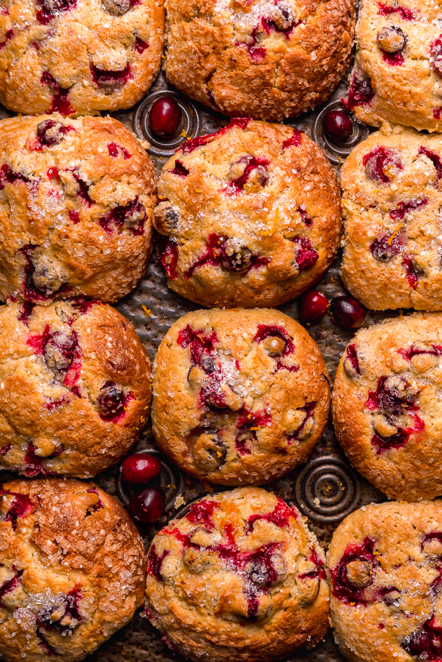 Cranberry orange muffins in a muffin pan with fresh cranberries and orange zest on top.