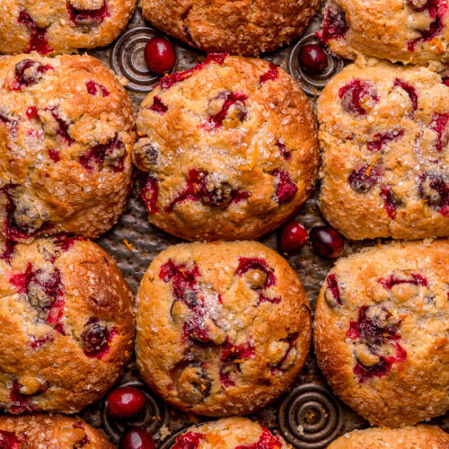 Cranberry orange muffins in a muffin pan with fresh cranberries and orange zest on top.