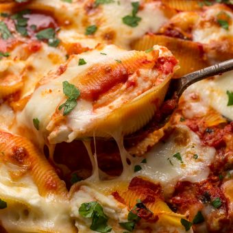 Stuffed shells being served out of a casserole dish with metal spoon.