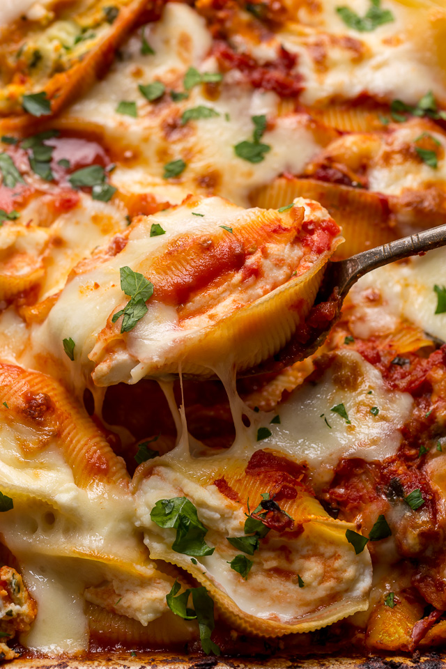 Stuffed shells being served out of a casserole dish with metal spoon.