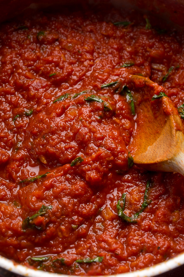 Homemade marinara sauce being stirred with a wooden spoon.