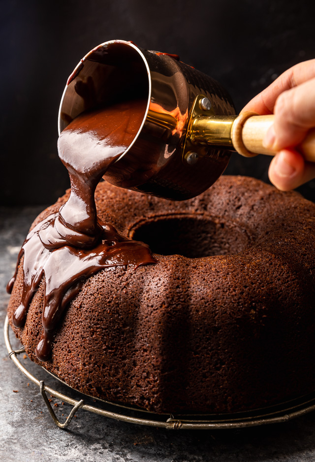 Chocolate ganache getting poured on top of a chocolate bundt cake.