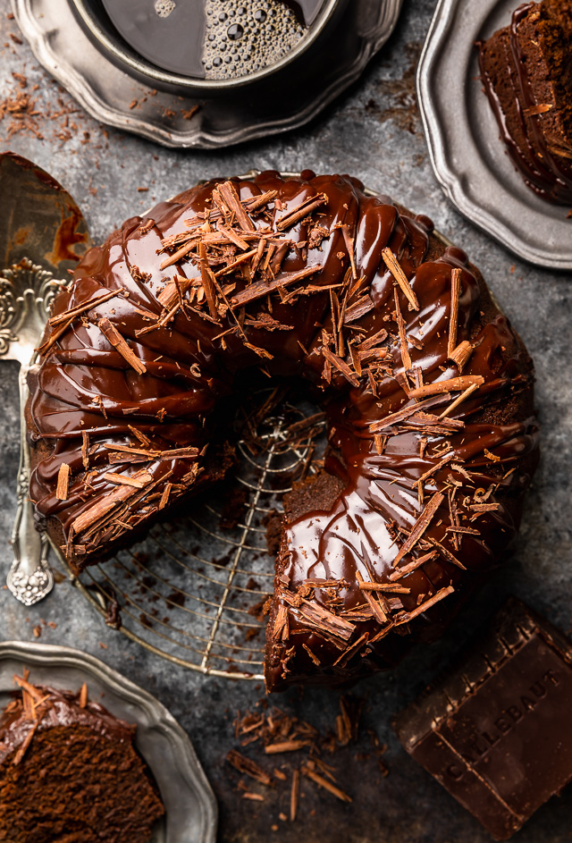 Chocolate bundt cake with chocolate glaze on top on a serving platter with a slice taken out.