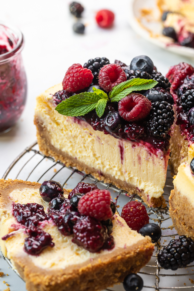 Slice of ricotta cheesecake on a cooling rack topped with fresh berries and berry sauce.