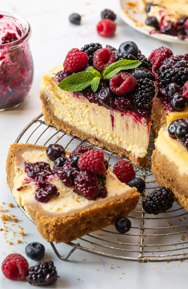 Slice of ricotta cheesecake on a cooling rack topped with fresh berries and berry sauce.