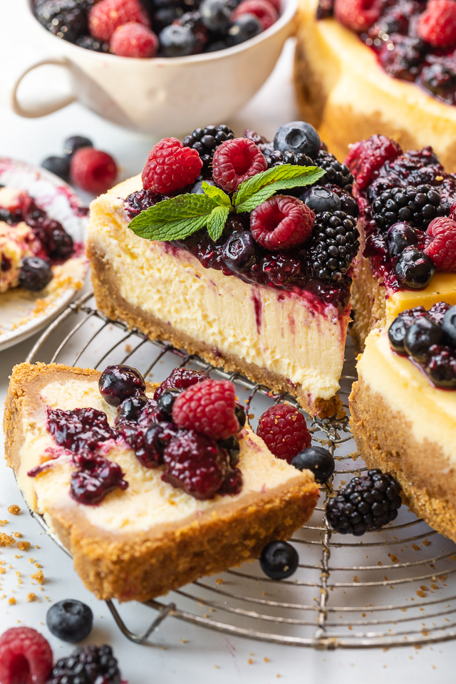 Slice of ricotta cheesecake with fresh berries and fresh berry sauce on top.