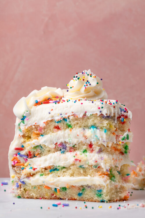 Slice of funfetti cake with sprinkles on the sides and on top of the cake.