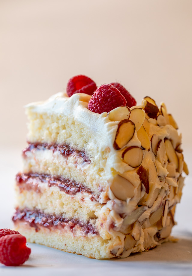 A slice of white chocolate raspberry cake with fresh berries on top.