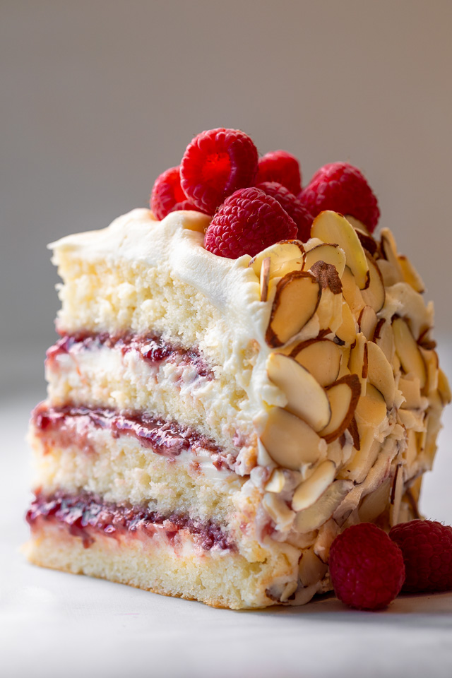 A slice of white chocolate raspberry cake with fresh berries on top.