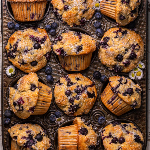 Muffin tin with banana blueberry muffins and tiny flowers.