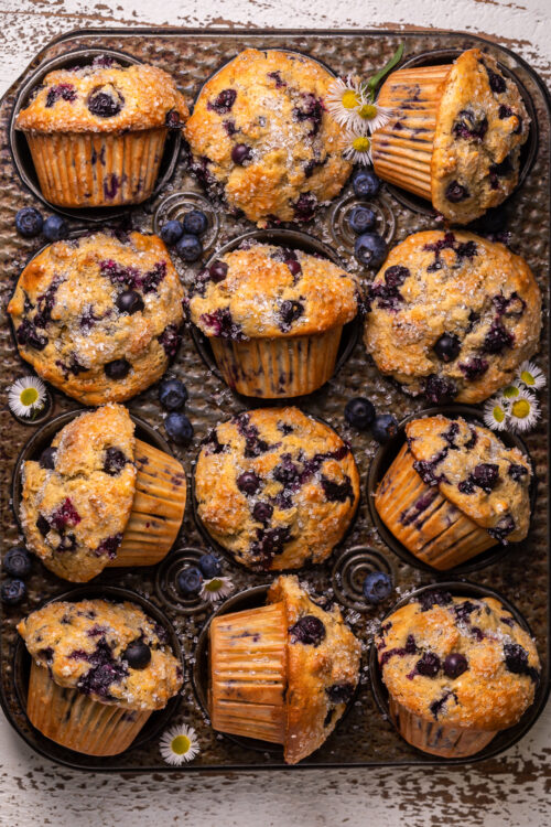 Muffin tin with banana blueberry muffins and tiny flowers.