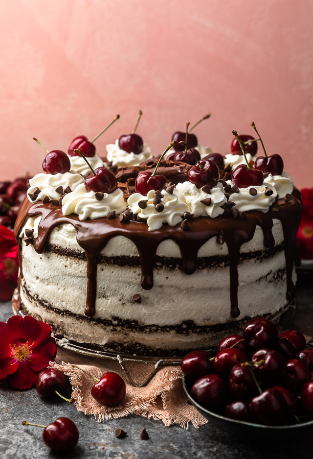 A whole black forest cake topped with whipped cream, chocolate chips, and fresh cherries.