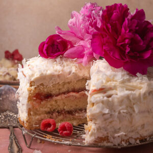 Slice of coconut cake on a white plate with a fork on the side.