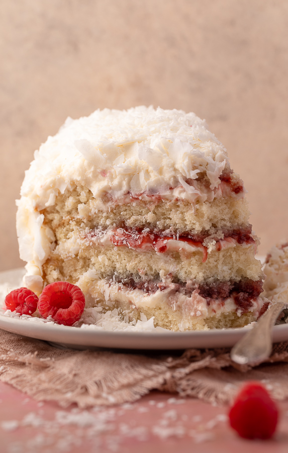 Slice of coconut cake on a white plate with a fork on the side.