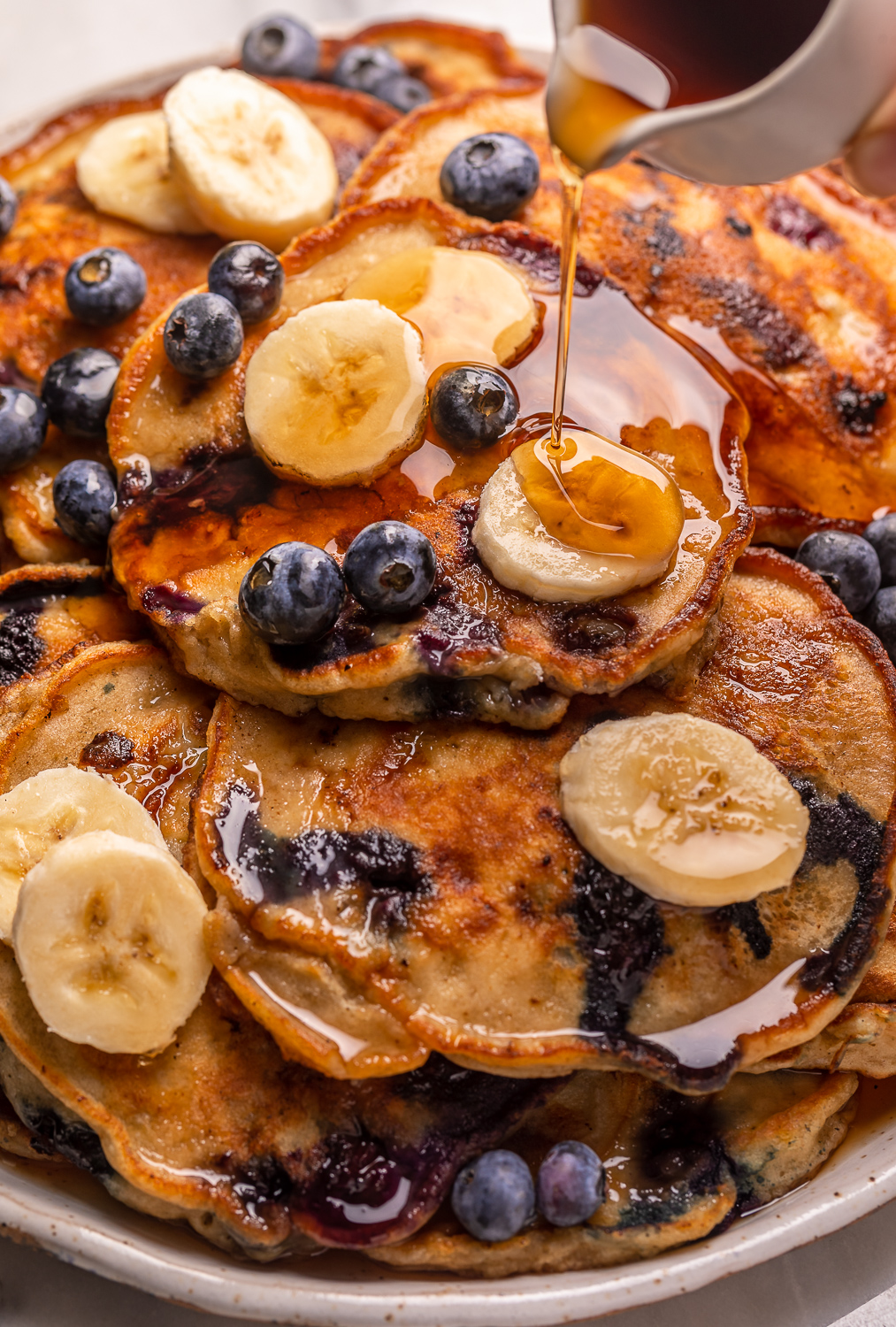 Ripe bananas and fresh blueberries make these Banana Blueberry Pancakes tender, fluffy, and flavorful! The pancake batter comes together in just minutes, and is quickly cooked to golden brown on a hot skillet. Top with maple syrup, extra blueberries, and banana slices for a beautiful breakfast at home!