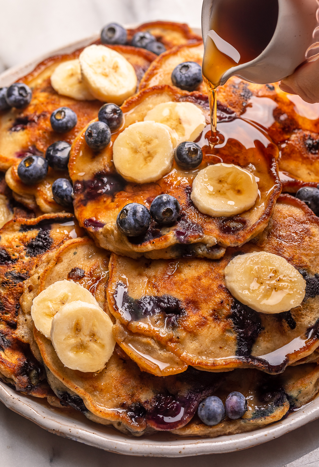 Ripe bananas and fresh blueberries make these Banana Blueberry Pancakes tender, fluffy, and flavorful! The pancake batter comes together in just minutes, and is quickly cooked to golden brown on a hot skillet. Top with maple syrup, extra blueberries, and banana slices for a beautiful breakfast at home!