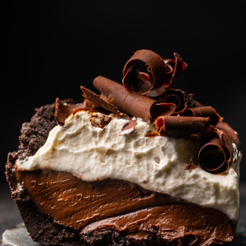 Chocolate pudding pie on a plate with whipped cream and chocolate shavings.