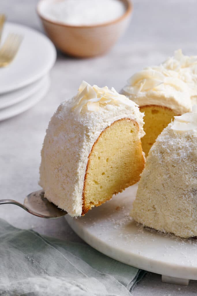 Coconut cake being lifted off platter with cake server.