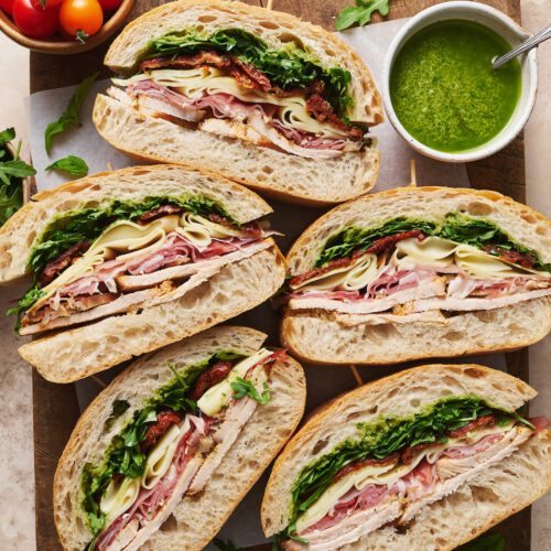 Italian turkey club sandwich sliced on a wooden cutting board.