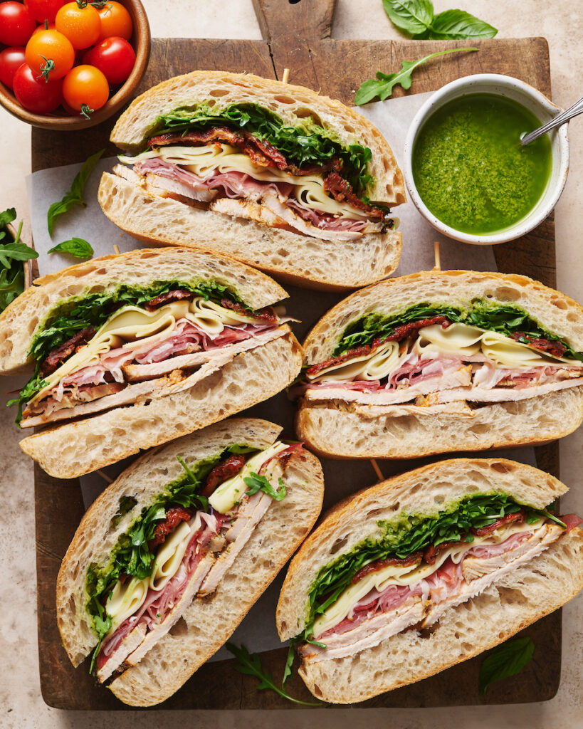 Italian turkey club sandwich sliced on a wooden cutting board.