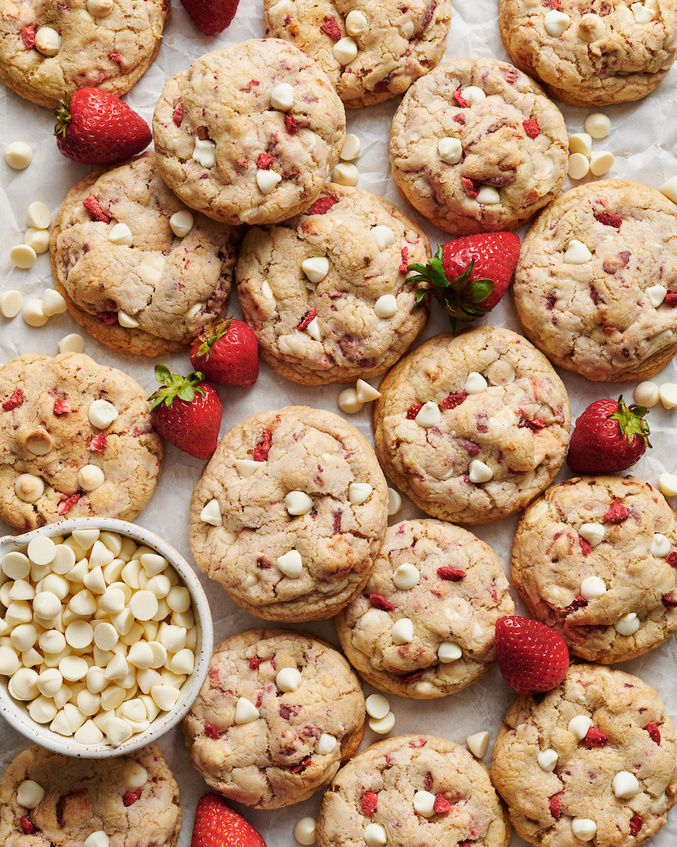 White chocolate strawberry cookies on a large baking sheet with fresh strawberries and white chocolate chips.