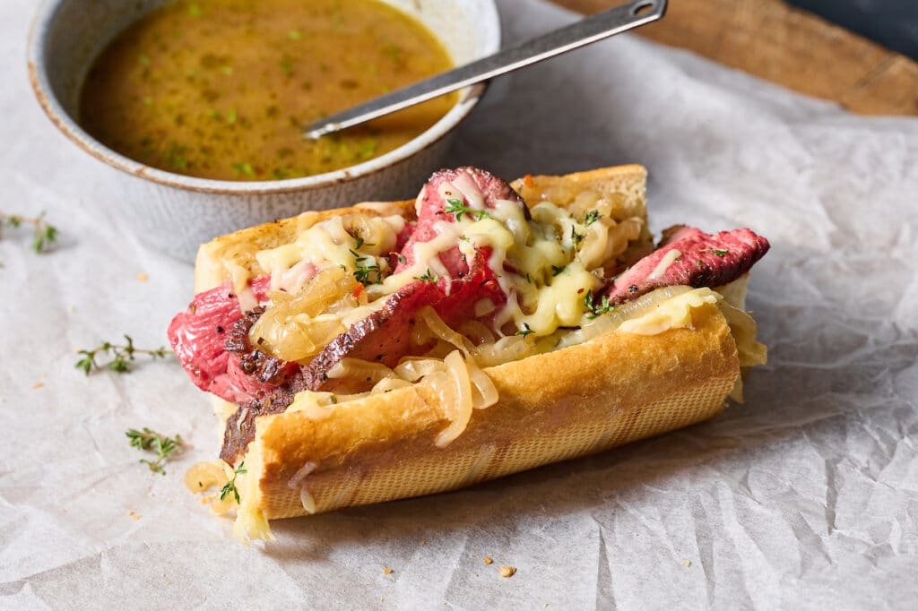 French dip sandwiches on white parchment paper with au jus on the side.
