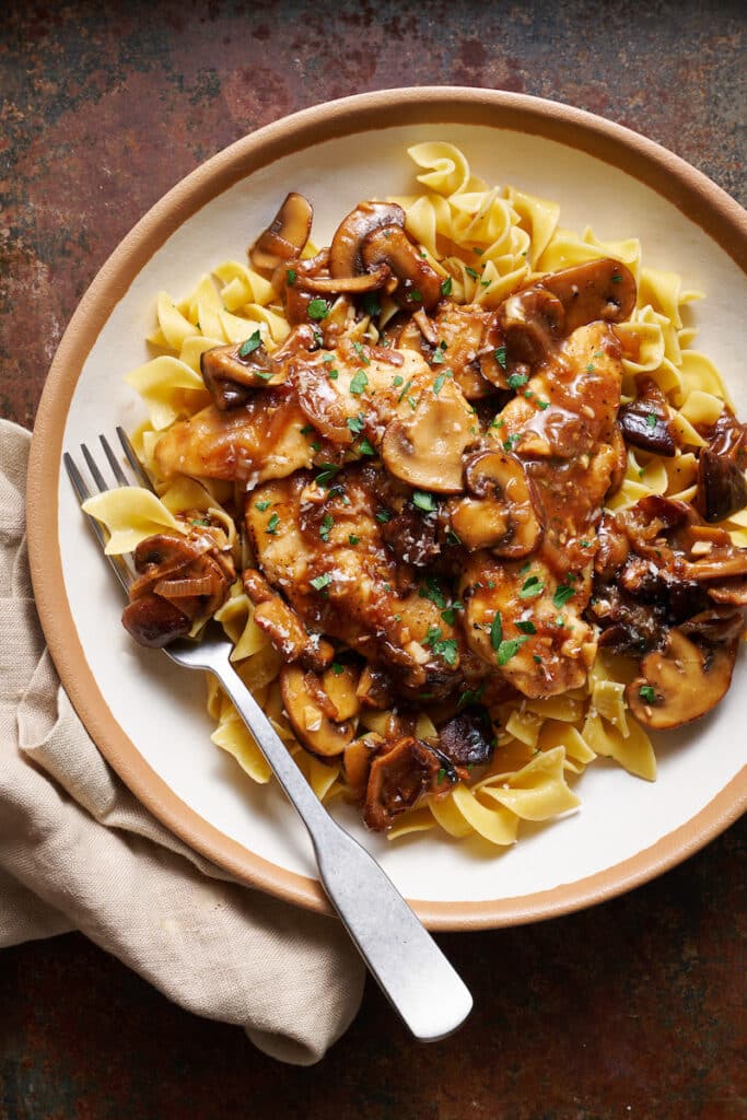 Plate of chicken marsala with mushrooms and creamy wine sauce on a brown plate.