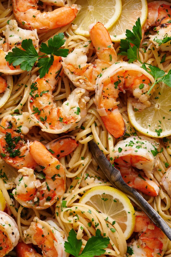 Close up of shrimp scampi in a big pot with extra lemon wedges and parsley on top.