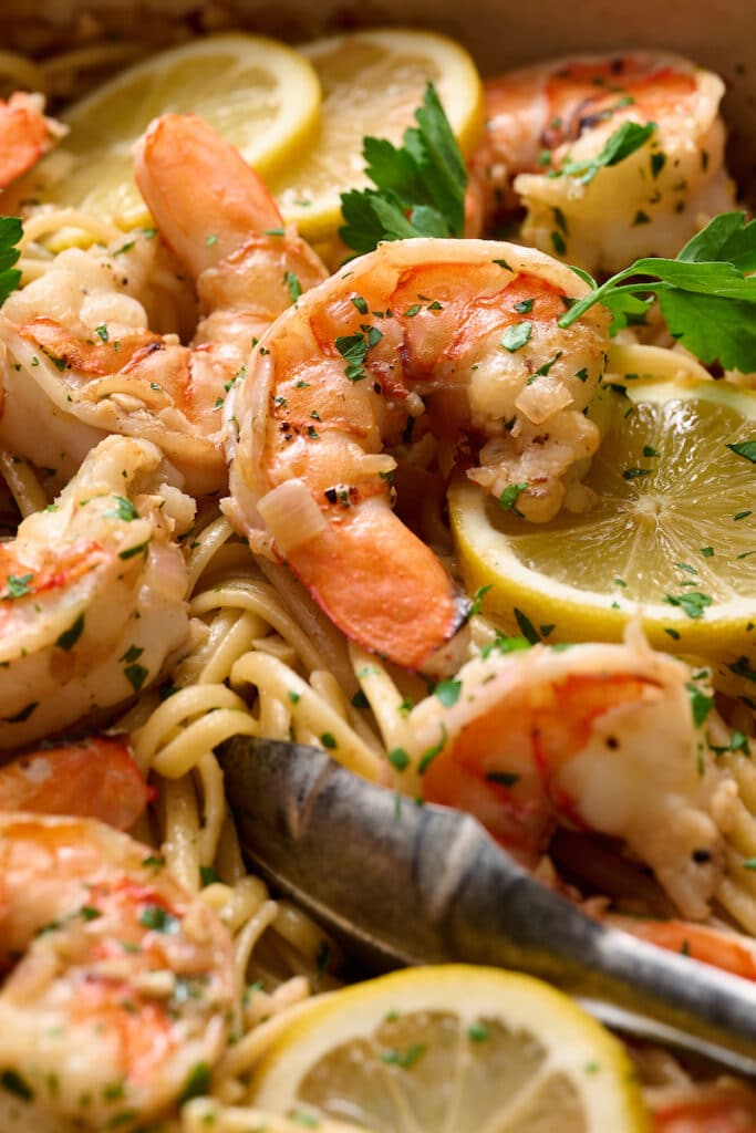 Shrimp scampi in a pot with lemon wedges on top.