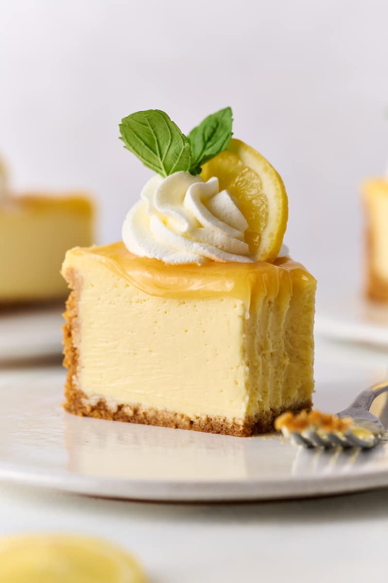 Slice of lemon cheesecake topped with lemon curd, whipped cream, and a sprig of mint.