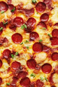 Baked pepperoni pizza with slices of pepperoni and fresh oregano sprigs on top.