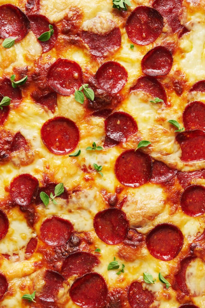 Baked pepperoni pizza with slices of pepperoni and fresh oregano sprigs on top.