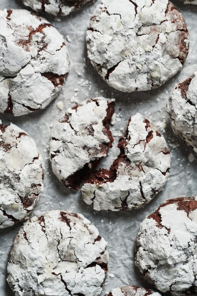chocolate crinkle cookies covered in powdered sugar coating on a white sheet of paper.
