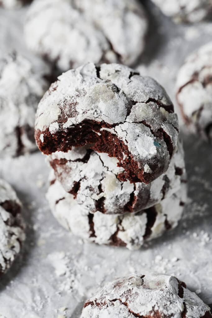 A stack of chocolate crinkle cookies with a bite taken out.