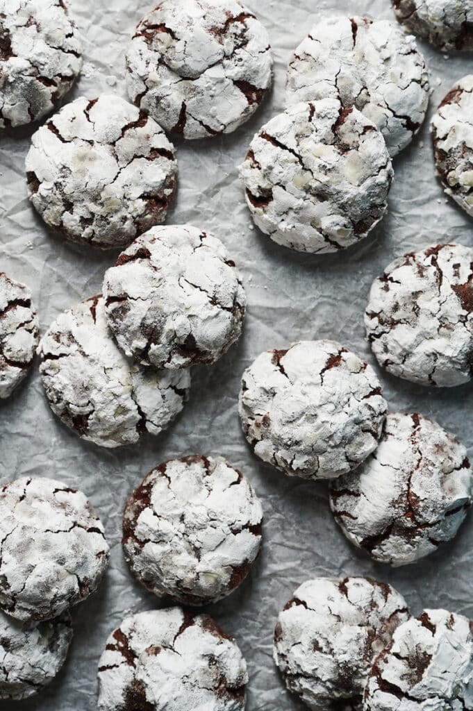 Chocolate crinkle cookies on a piece of white parchment paper.