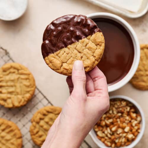 Hand holding a peanut butter cookie that's been dipped in chocolate.