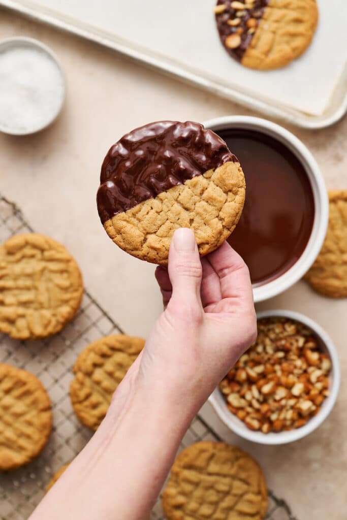Hand holding a peanut butter cookie that's been dipped in chocolate.