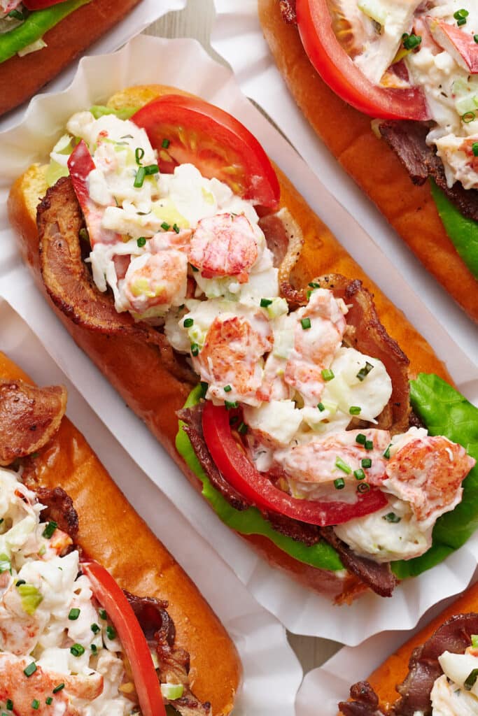 Learn how to make lobster rolls with this easy lobster roll recipe! The lobster salad contains cooked lobster meat, lemon juice, melted butter, mayo, and fresh herbs. The lobster mixture is piled high on toasted split top buns and topped with bacon, lettuce, and tomato! We love to serve these with crunchy potato chips and ice cold beer.