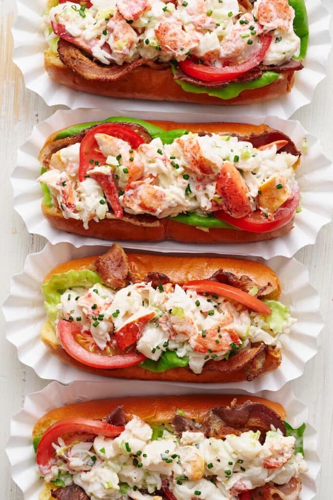 Learn how to make lobster rolls with this easy lobster roll recipe! The lobster salad contains cooked lobster meat, lemon juice, melted butter, mayo, and fresh herbs. The lobster mixture is piled high on toasted split top buns and topped with bacon, lettuce, and tomato! We love to serve these with crunchy potato chips and ice cold beer.
