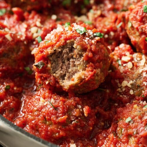 Meatballs in a dutch oven with marinara sauce and cheese on top.