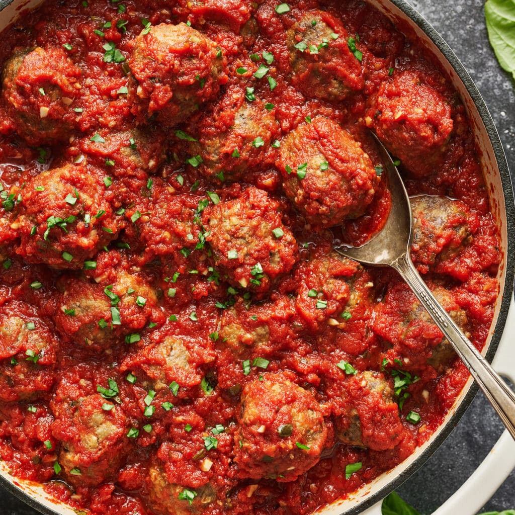 Meatballs with marinara sauce being scooped out of a pot.