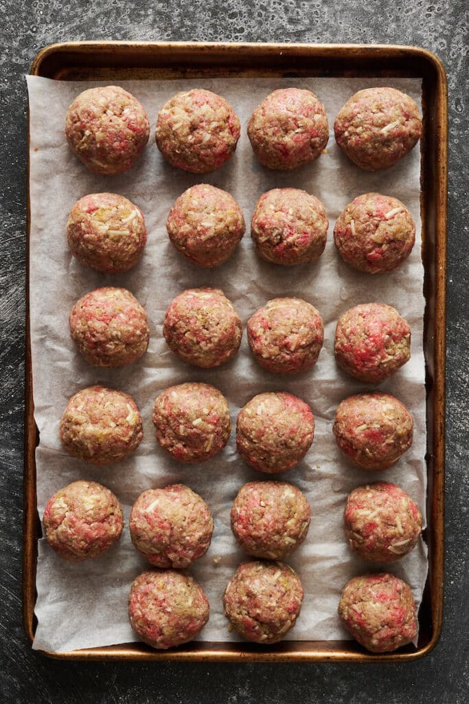 Rolled meatballs on a large parchment paper lined baking sheet.