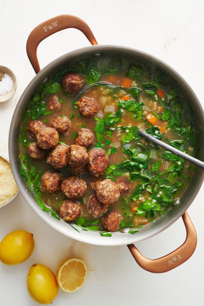 Adding mini meatballs and spinach to soup pot.