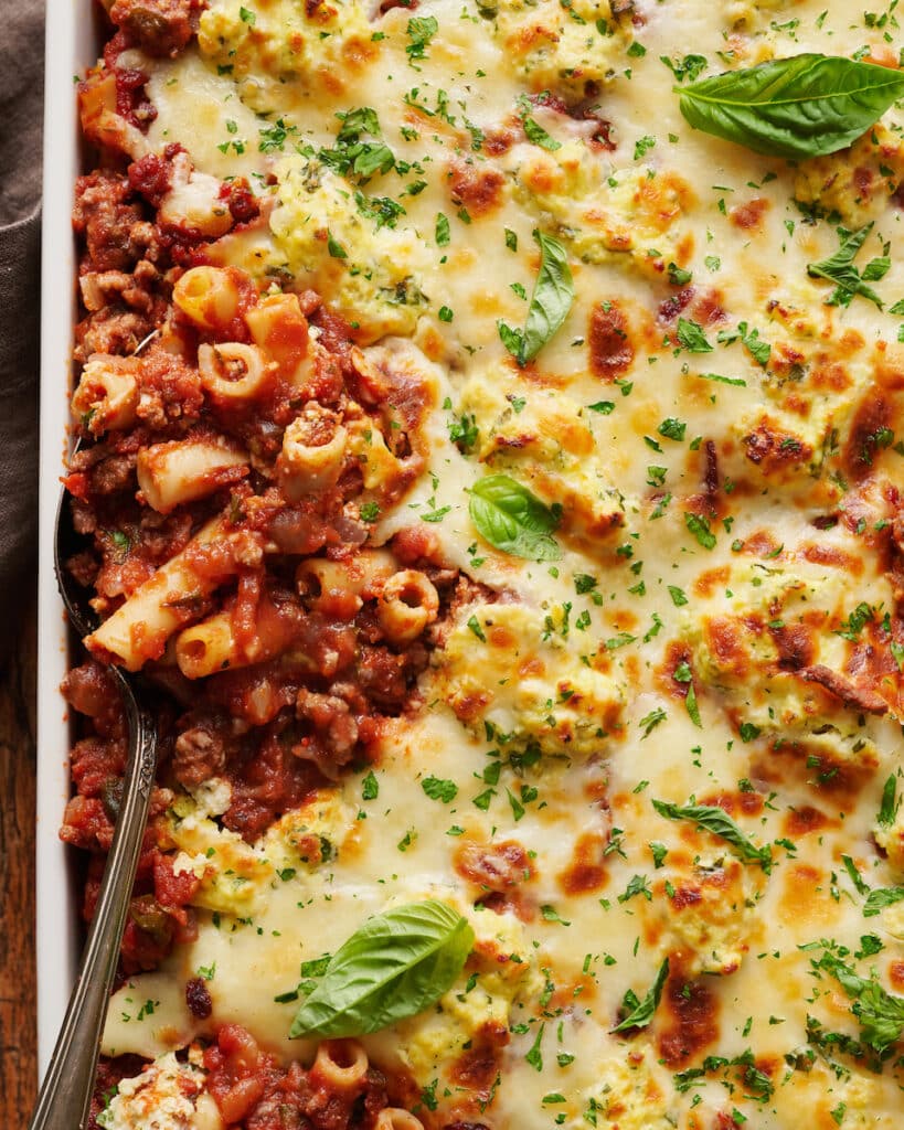 Baked ziti in baking dish being scooped out with a large spoon.