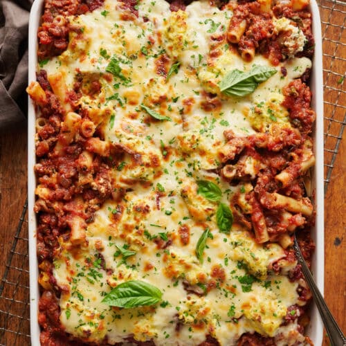 Casserole dish full of baked ziti topped with cheese and basil.