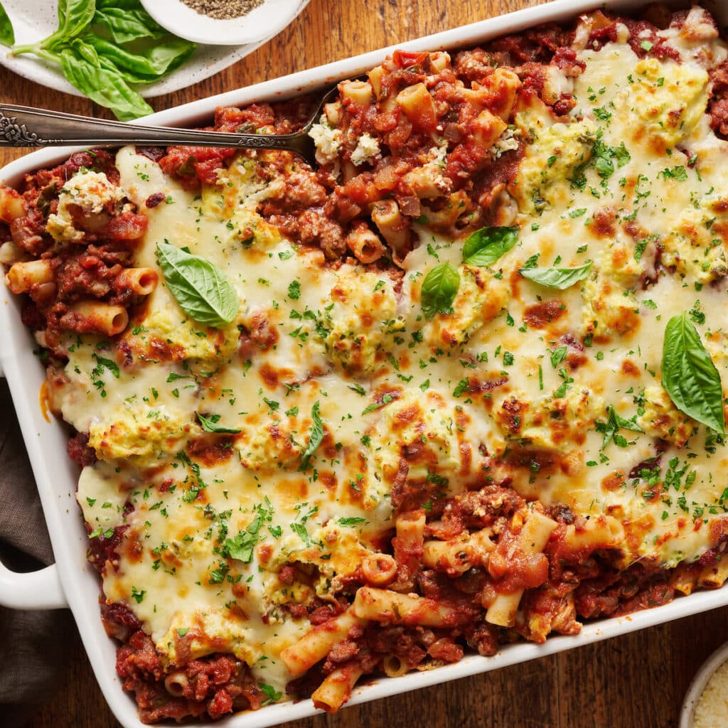 Casserole dish full of baked ziti topped with cheese and basil.