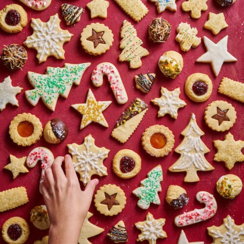 Christmas cookies on a red table with a hand picking up a cookie.