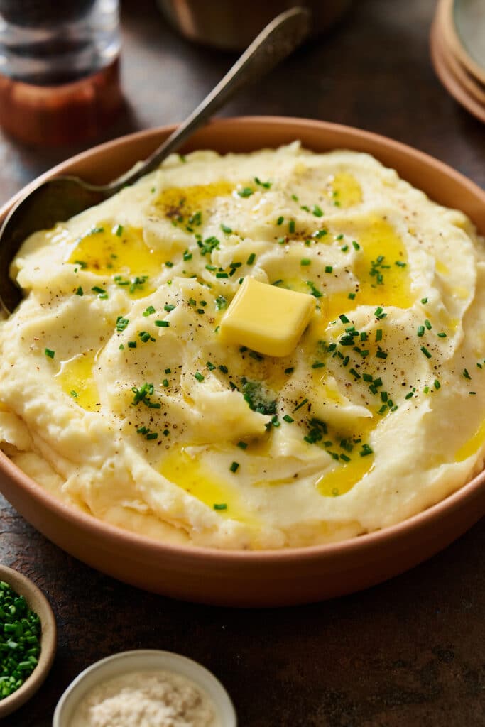 A bowl of fluffy mashed potatoes topping with melted butter and chives.