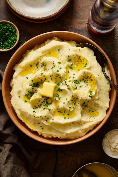 Fluffy sour cream Mashed Potatoes in a large bowl topped with melted butter and chives.